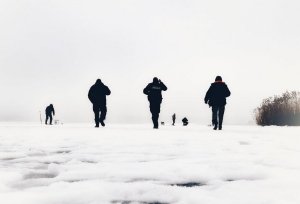 Mężczyźni idący po lodzie, w tym policjant, w tle wędkarze
