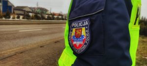 Napis na mundurze Komenda Powiatowa Policji w Grajewie, w tle zabudowania, policjant ruchu drogowego